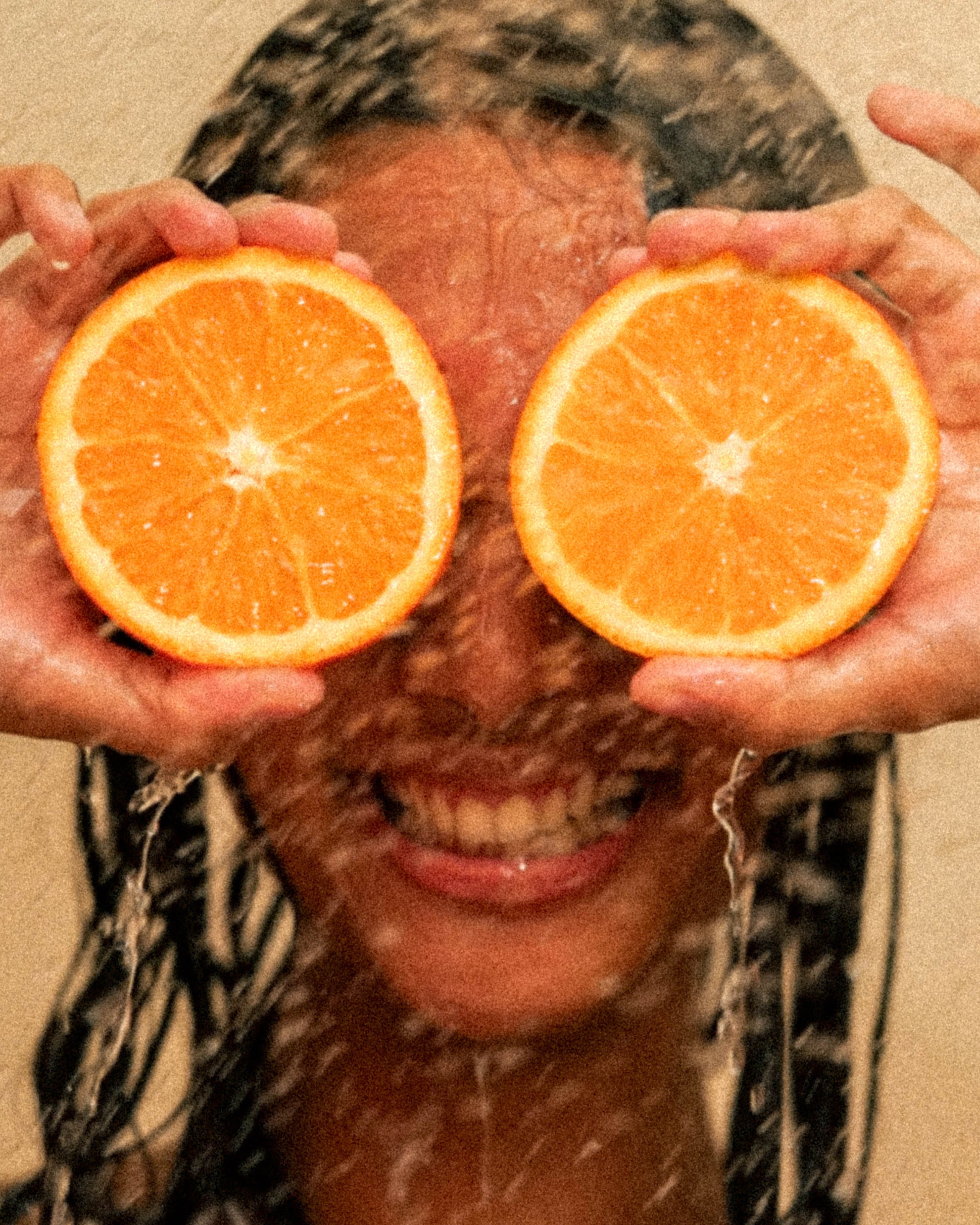 Person_holding_two_halves_of_an_orange_in_front_of_their_eyes_with_a_beige_background.jpg